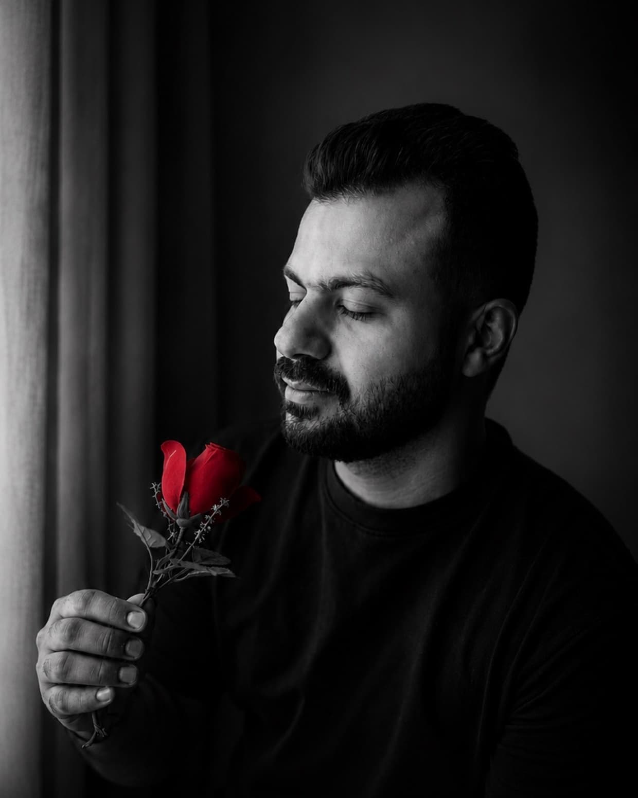 Omar Hassan, holding a red rose, in a black-and-white portrait.